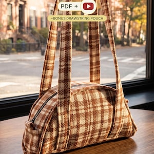Puede incluir: Un bolso de tela a cuadros marrón y crema con dos correas largas para el hombro y cierre de cremallera superior. El bolso muestra el texto PDF + y +BONUS DRAWSTRING POUCH superpuesto, indicando un patrón digital y un accesorio extra.