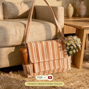 May include: A rectangular shoulder bag made of orange and white striped fabric with a fold-over flap and a side pocket containing a solid brown cylindrical bottle. A bouquet of white daisies with yellow centres is tucked into the side pocket.