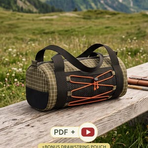 Könnte beinhalten: Eine zylindrische, olivgrüne Reisetasche mit weißem Gittermuster, schwarzen Nylongurten und einem schwarzen Netzeinsatz auf der Vorderseite, der mit einer leuchtend orangefarbenen elastischen Kordel gesichert ist. Der Boden ist schwarz.