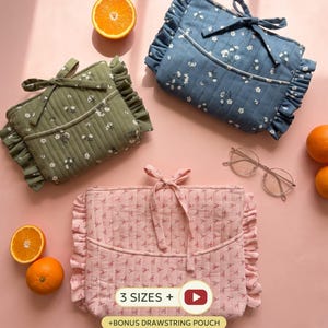 May include: Three quilted pouches in sage green, dusty blue, and soft pink, each featuring a floral pattern, ruffled edges, and a tie closure. The pink pouch displays the text 3 SIZES + and +BONUS DRAWSTRING POUCH. Oranges and glasses are nearby.
