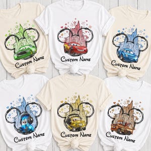 K&ouml;nnte beinhalten: Sechs kurz&auml;rmelige T-Shirts in Wei&szlig; und Naturfarben, jedes mit einer Grafik eines Disney Cars-Charakters in einer Micky-Maus-Ohren-Silhouette mit Schloss-Hintergrund, bunten Sternen und dem unter dem Design gedruckten Text Custom Name.