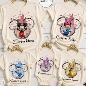 May include: A collection of five cream-colored shirts and one bodysuit featuring Disney character graphics. Each garment displays a character inside a black circular outline with a castle background, stars, and the text Custom Name below.