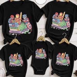 Puede incluir: Una colecci&oacute;n de cinco prendas negras, incluyendo cuatro camisetas y un body para beb&eacute;, cada una con un estampado gr&aacute;fico de los superh&eacute;roes de dibujos animados Spider-Man, Iron Man, Captain America y Hulk sentados sobre una pila de libros con el texto Avengers Assemble.
