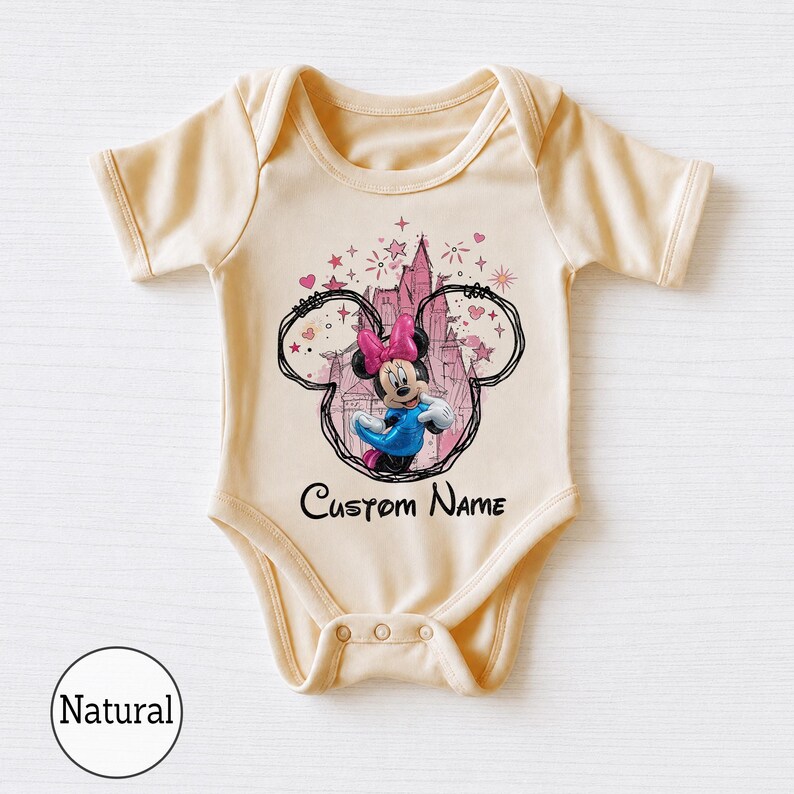 May include: A light beige short-sleeve baby bodysuit featuring a graphic of Minnie Mouse in a blue dress and pink bow, framed by a black outline of Mickey ears and a pink castle. The text Custom Name is printed in black below the graphic.
