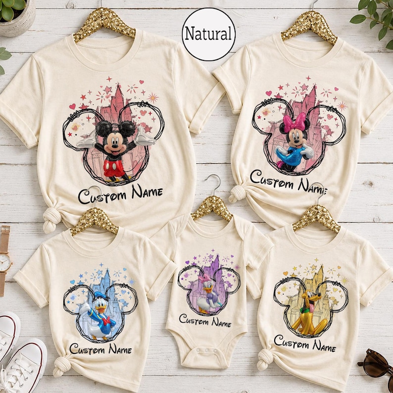 May include: A collection of five cream-colored shirts and one bodysuit featuring Disney character graphics. Each garment displays a character inside a black circular outline with a castle background, stars, and the text Custom Name below.