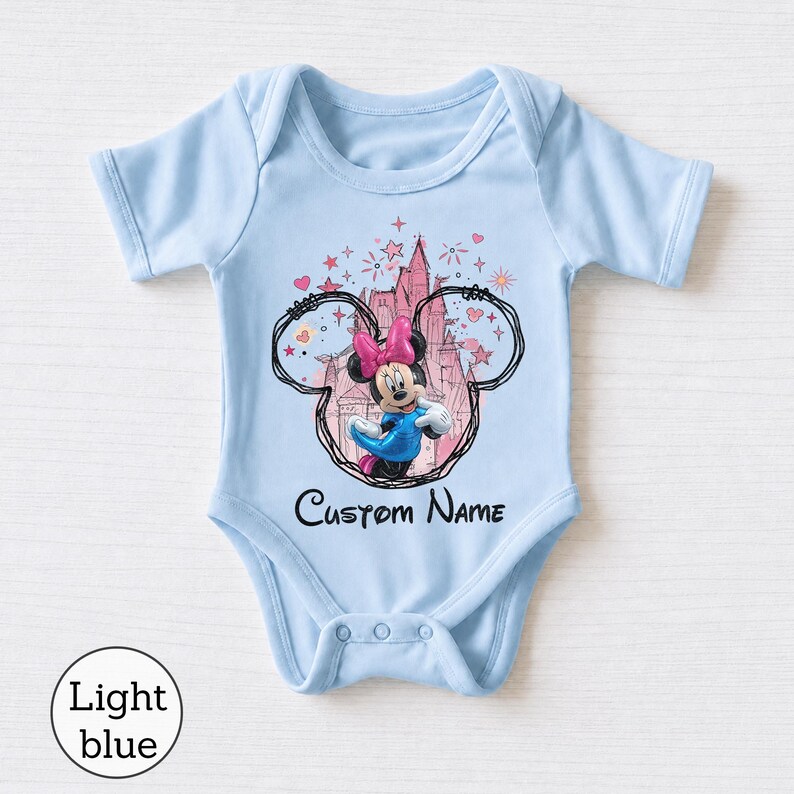 May include: A light blue baby bodysuit featuring a graphic of Minnie Mouse inside a black outline of Mickey Mouse ears. Behind the character is a pink castle illustration with stars and hearts. The text Custom Name is printed in black below.