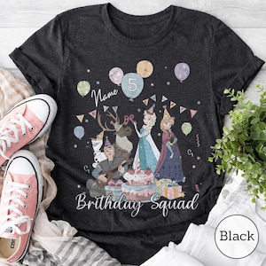 Op de afbeelding: Een donkergrijs t-shirt met een grafische print van geanimeerde figuren, waaronder een sneeuwpop, een rendier en twee figuren in jurken, omringd door ballonnen, een verjaardagstaart en cadeaus. De tekst luidt Name, 5 en Birthday Squad.