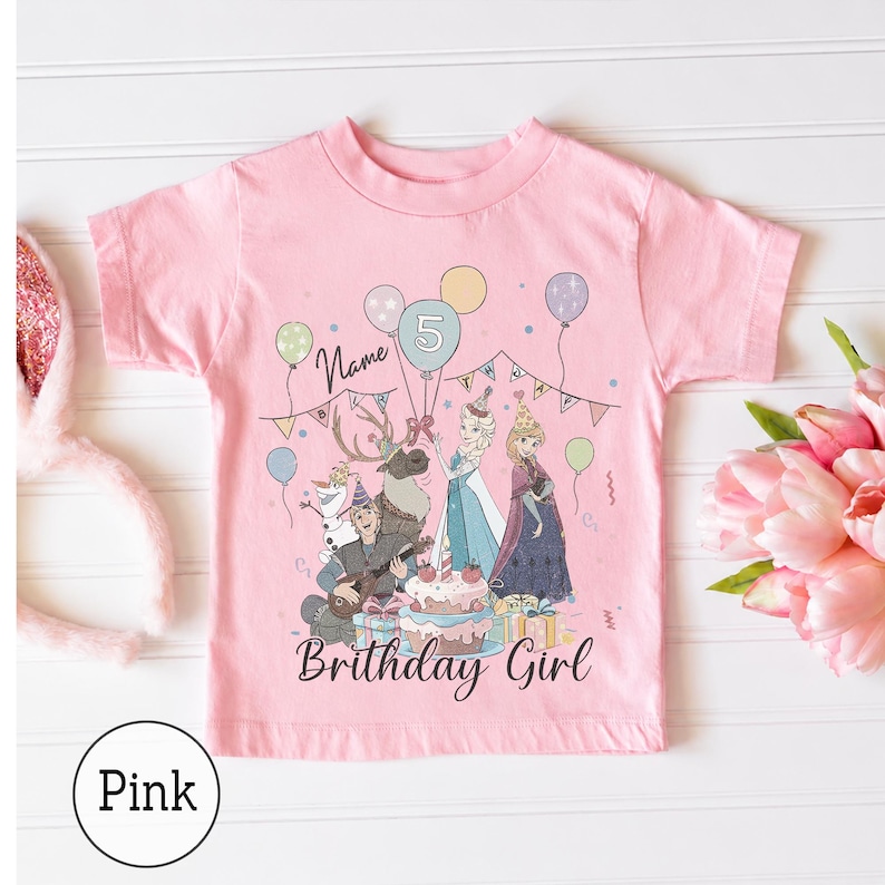 Op de afbeelding: Een lichtroze T-shirt met korte mouwen en een grafische print van personages uit Frozen, waaronder Elsa, Anna, Olaf en Sven. Het ontwerp bevat een verjaardagstaart, ballonnen, een slinger, het cijfer 5 en de tekst Name Birthday Girl.
