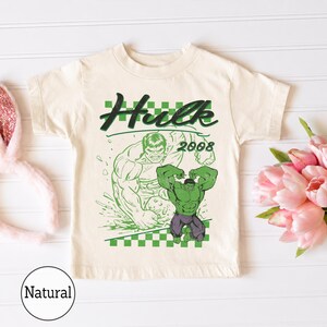 Pu&ograve; includere: Una t-shirt a maniche corte color crema con una stampa grafica verde del personaggio Hulk. Il design include il testo Hulk e 2008, un motivo a scacchi e una grande illustrazione del personaggio in una posa dinamica sulla parte anteriore.