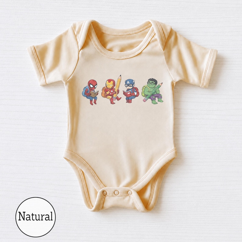 May include: A natural-colored short-sleeve baby bodysuit featuring a graphic print of four cartoon superheroes. The characters include Spider-Man reading a book, Iron Man holding a large pencil, Captain America reading, and the Hulk holding a pencil.
