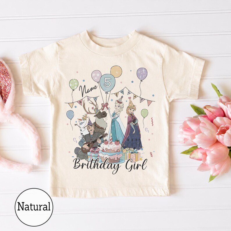 Op de afbeelding: Een cr&egrave;mekleurig T-shirt met korte mouwen en een grafische print van personages uit Frozen, waaronder Elsa, Anna, Kristoff, Sven en Olaf. Het ontwerp bevat ballonnen, een verjaardagstaart, feesthoedjes en de tekst Name en Brithday Girl.