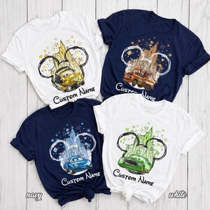 K&ouml;nnte beinhalten: Vier kurz&auml;rmelige T-Shirts in Wei&szlig; und Marineblau mit grafischen Drucken von Cartoon-Autos vor Schloss-Silhouetten, die von Mickey-Maus-Ohren umrandet sind. Jedes Design enth&auml;lt Sterne, Herzen und den Schriftzug Custom Name in schwarzer Schrift.