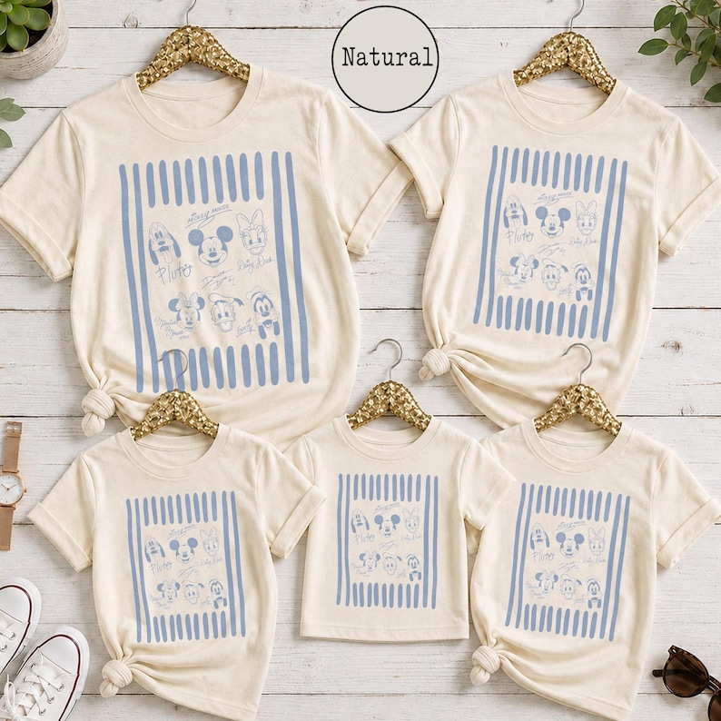 May include: Five natural-colored t-shirts with short sleeves and crew necks, each featuring a central graphic of blue vertical stripes framing line-art illustrations of cartoon characters and the text Natural printed in a circular badge above.