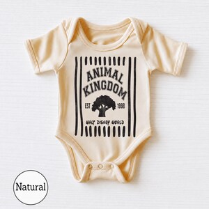 Pu&ograve; includere: Un body per neonati a maniche corte di colore naturale con una stampa grafica nera. Il design include strisce verticali, il testo ANIMAL KINGDOM, EST 1998 e WALT DISNEY WORLD, centrato attorno alla sagoma di un grande albero.