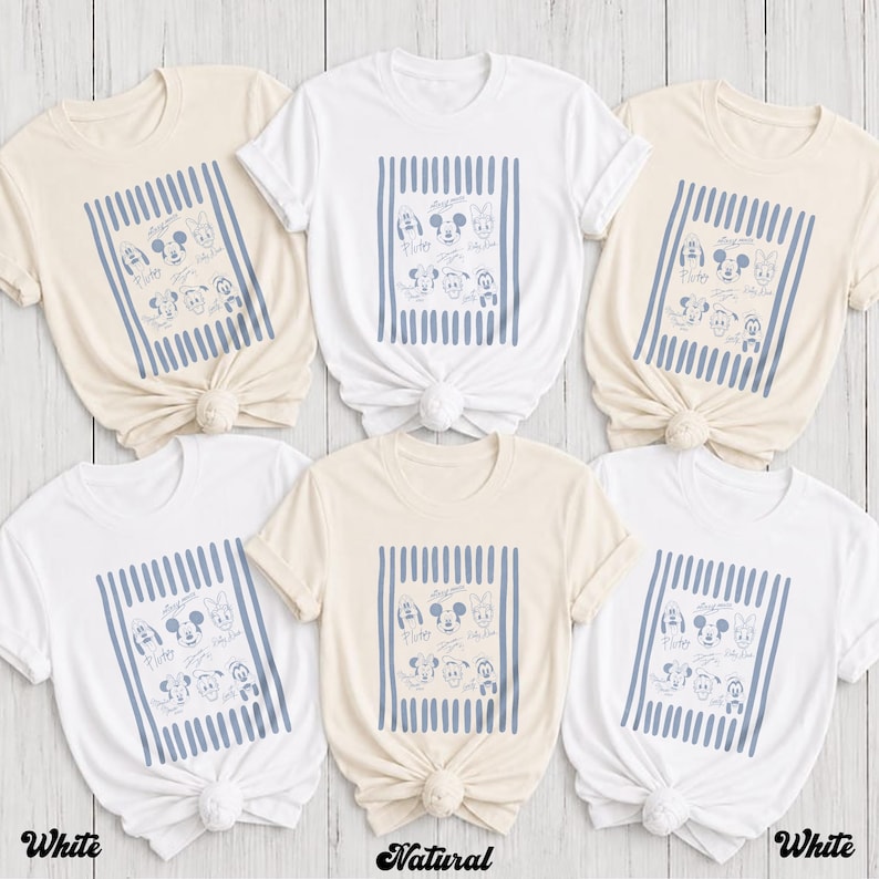 May include: A collection of six short-sleeved t-shirts in white and natural beige. Each shirt features a central rectangular graphic with vertical blue stripes and line-art illustrations of various cartoon characters with their names printed below.
