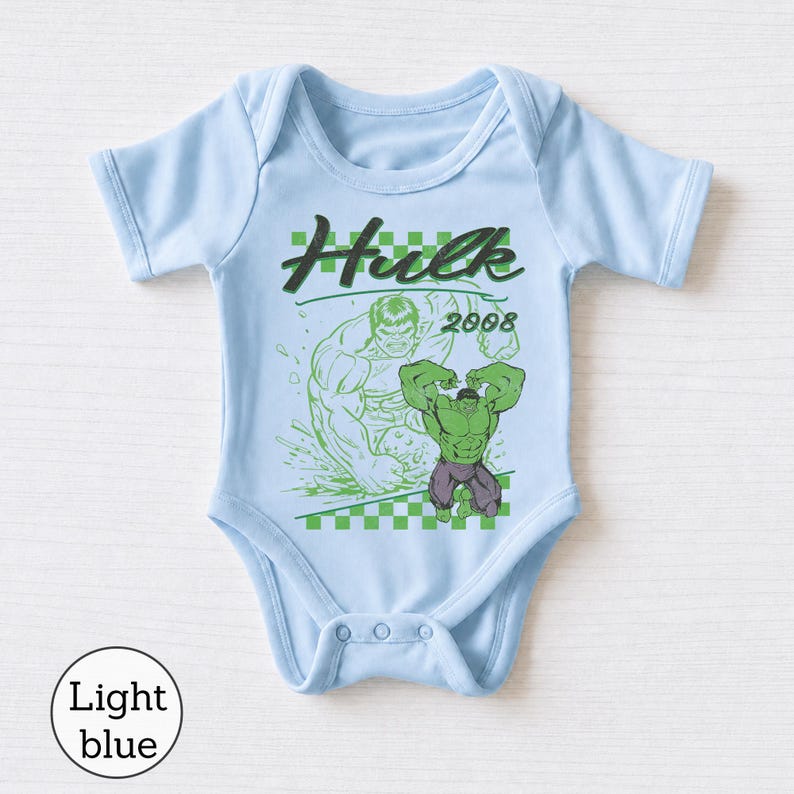 Pu&ograve; includere: Un body per neonati azzurro con una stampa grafica di Hulk e il testo "Hulk 2008" sopra un motivo a scacchi verde e bianco. Il design include una grande illustrazione verde del personaggio e un contorno verde pi&ugrave; piccolo.