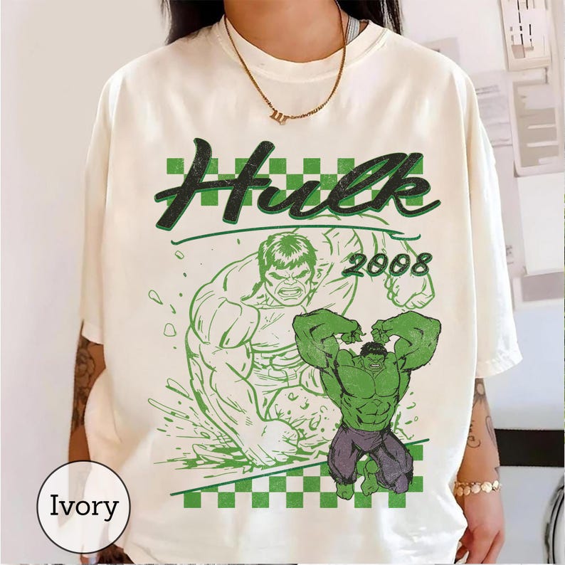 Pu&ograve; includere: Una t-shirt color avorio con una stampa grafica verde di Hulk. Il design include il testo Hulk e 2008, uno sfondo a scacchi e una grande illustrazione del personaggio che flette i muscoli. La maglietta presenta un girocollo.
