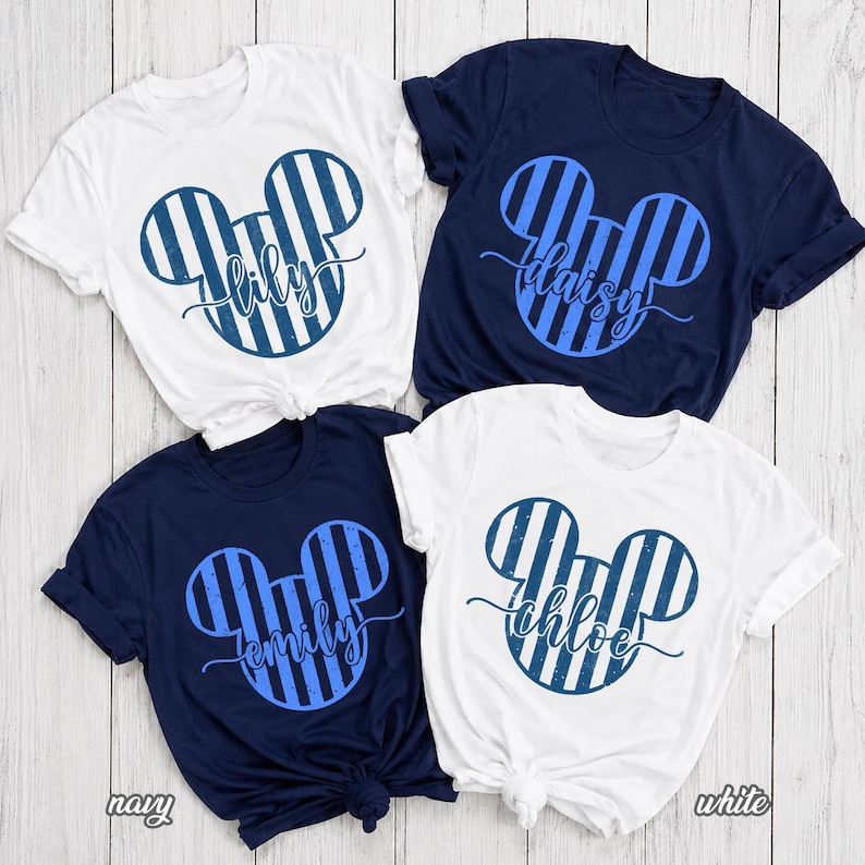 K&ouml;nnte beinhalten: Vier kurz&auml;rmelige T-Shirts mit Rundhalsausschnitt in Wei&szlig; und Marineblau. Jedes Shirt zeigt eine gro&szlig;e Mausohren-Silhouette mit vertikalen blauen Streifen und einer abgenutzten Textur. Die Namen Lily, Daisy, Emily und Chloe sind in Schreibschrift gedruckt.