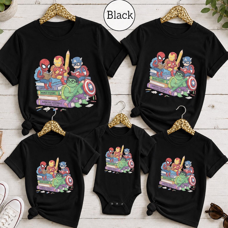 Puede incluir: Una colecci&oacute;n de cinco prendas negras, incluyendo cuatro camisetas y un body para beb&eacute;, cada una con un estampado gr&aacute;fico de los superh&eacute;roes de dibujos animados Spider-Man, Iron Man, Captain America y Hulk sentados sobre una pila de libros con el texto Avengers Assemble.