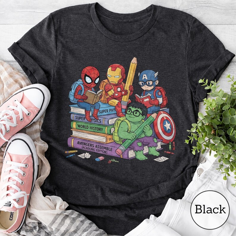 Puede incluir: Una camiseta gris carb&oacute;n oscuro con un estampado gr&aacute;fico de superh&eacute;roes de dibujos animados, Spider-Man, Iron Man, Captain America y Hulk, sentados sobre una pila de libros. Los libros est&aacute;n etiquetados como Super Physics, World History y Avengers Assemble.