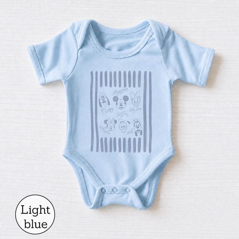 May include: A light blue baby bodysuit featuring short sleeves and a crew neckline. The center of the garment displays a gray graphic print of various Disney character faces and signatures framed by vertical stripes, including Mickey Mouse and Pluto.