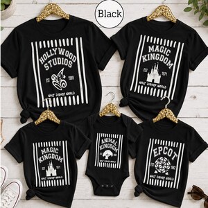 Pu&ograve; includere: Una collezione di cinque magliette nere a maniche corte e un body con stampe grafiche bianche dei parchi Walt Disney World. Ogni capo presenta strisce verticali, nomi dei parchi, anni di fondazione e simboli iconici come il castello e il globo.