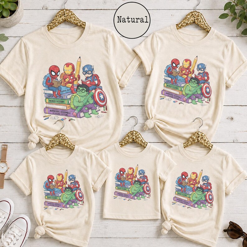 Puede incluir: Cinco camisetas de color natural con un estampado gr&aacute;fico de superh&eacute;roes de dibujos animados, incluyendo a Spider-Man, Iron Man, Capit&aacute;n Am&eacute;rica y Hulk sentados sobre una pila de libros. El texto "Natural" aparece en un c&iacute;rculo.