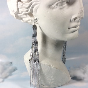May include: Silver chain earrings with a fringe design. The earrings are long and dangle from the earlobes.