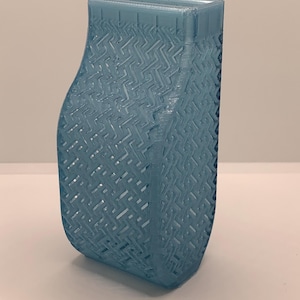 Könnte beinhalten: Ein durchscheinendes, hellblaues 3D-gedrucktes Objekt mit einer geschwungenen Vorderseite und einer flachen Rückseite. Die Oberfläche weist ein sich wiederholendes geometrisches Gittermuster mit offenen Zwischenräumen auf, und die Oberkante ist offen.