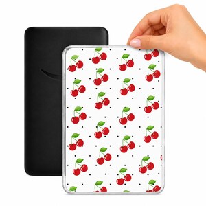 May include: A black e-reader next to a clear case with a cherry pattern. The case features a white background with a repeating pattern of red cherries and green leaves, interspersed with black dots.