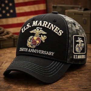 May include: A black baseball cap featuring the embroidered text U.S. MARINES and 250TH ANNIVERSARY in gold thread. The front displays a gold and red Eagle, Globe, and Anchor emblem. The side panel has a digital camouflage pattern and a rectangular patch.