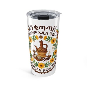 May include: A white stainless steel tumbler with a clear lid featuring a graphic of a traditional Ethiopian coffee pot, small cups, and yellow sunflowers. The text reads "ETHIOPIAN NEW YEAR" in English and Amharic script, accented with green, yellow, and red ribbons.