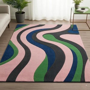 Könnte beinhalten: Ein rechteckiger Teppich mit einem wiederkehrenden Muster aus wellenförmigen, fließenden Streifen in den Farben zartes Rosa, tiefes Marineblau, Waldgrün und Anthrazit. Der Teppich hat eine strukturierte, getuftete Oberfläche mit Farbblöcken.