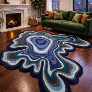 Può includere: Un tappeto dalla forma irregolare caratterizzato da un motivo concentrico e fluido di colori stratificati, tra cui blu navy profondo, blu reale, verde acqua, azzurro, grigio e lavanda. Il tappeto presenta una consistenza morbida.
