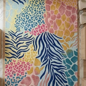 Könnte beinhalten: Ein rechteckiger Teppich mit einem Patchwork aus Tiermustern, darunter blaue Zebrastreifen, rosa und gelbe Giraffenflecken sowie blaue und rosa Leopardenflecken. Das Design kombiniert verschiedene Texturen und Farben in einem gemusterten Layout.