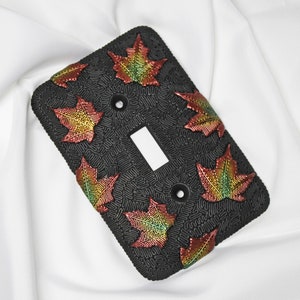May include: Black light switch cover with a raised design of colorful fall leaves. The leaves are red, orange, yellow, and green.