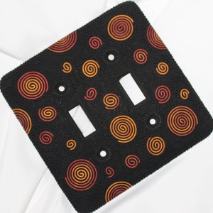 May include: A black light switch cover with a double switch and a pattern of orange and red spiral designs.