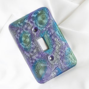 May include: A light switch cover with a decorative design of swirling circles in shades of purple, blue, and green.