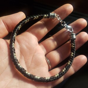 May include: A braided bracelet featuring dark brown and light blonde strands woven together in a tight pattern. The bracelet is finished with silver-toned metal end caps and a lobster claw clasp, creating a secure closure for the circular band.
