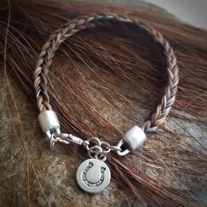 May include: A braided brown and white horsehair bracelet with a silver horseshoe charm.