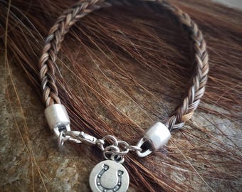 May include: A braided brown and white horsehair bracelet with a silver horseshoe charm.