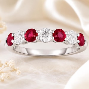 Peut inclure: Une bague argentée ornée d'une rangée de sept pierres précieuses rondes alternées. Le design comprend quatre rubis rouge vif et trois diamants blancs étincelants sertis sur une bande en métal poli avec un style de sertissage à griffes.
