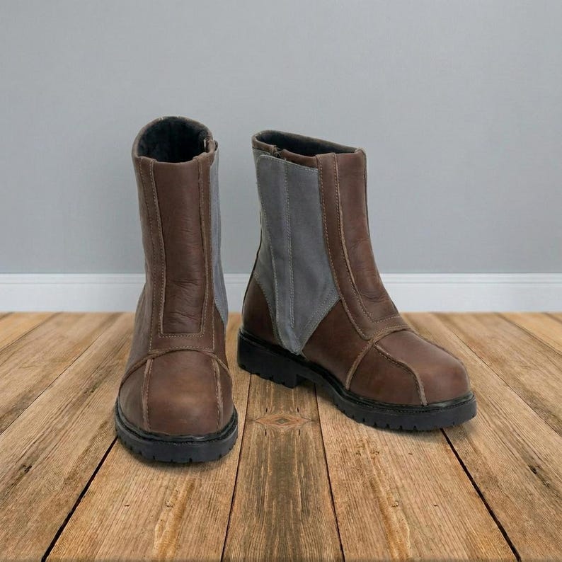 May include: A pair of mid-calf boots featuring brown leather construction with contrasting gray fabric side panels. The boots have a rounded toe, a vertical seam detail along the front, and a thick black lug sole with a defined heel.