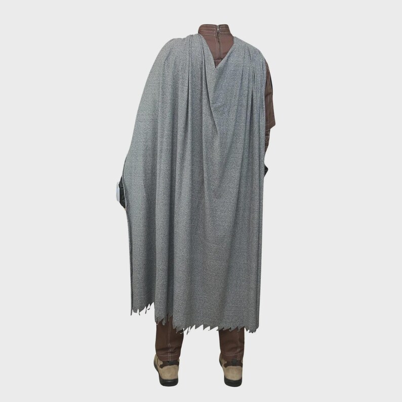 May include: A long, heather gray cape with a textured fabric finish, worn over a brown high-neck garment and brown trousers. The cape features a straight, unhemmed bottom edge and drapes over the shoulders, paired with brown shoes.