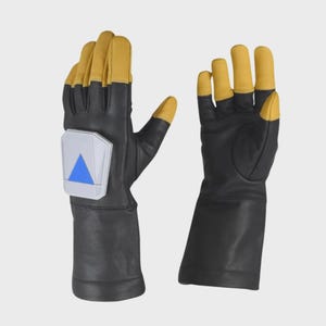 May include: A pair of black and tan gloves with long cuffs. The left glove features a white, pentagonal-shaped rigid plate on the back of the hand, which displays a bright blue triangle pointing downward. The fingers are tipped in tan.