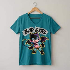 Könnte beinhalten: Ein blaugrünes V-Ausschnitt-T-Shirt mit einer Grafik einer Zeichentrickfigur, die eine schwarze Fledermausmaske, Flügel und ein rosa Brustemblem trägt. Die Figur hält eine Peitsche und der Text "BAD GIRL" ist in Schwarz über ihr abgebildet.