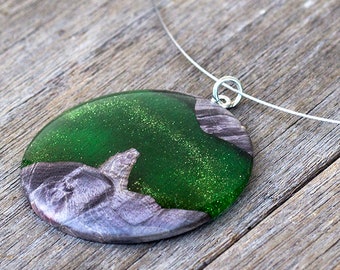 May include: A round green and silver resin pendant necklace with a silver chain. The pendant has a green glitter finish and a silver swirl design.