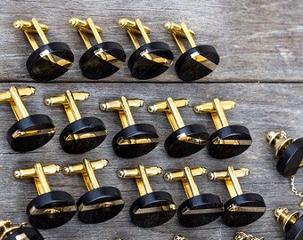 May include: A set of 15 gold cufflinks and 5 tie tacks with black and gold accents. The cufflinks and tie tacks have a round shape with a black background and a gold stripe.