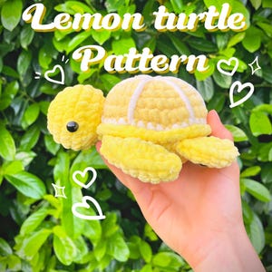 May include: A handmade yellow crochet turtle with white accents and a black eye. The text "Lemon turtle Pattern" is displayed above the turtle. The turtle is held in front of a green leafy background.