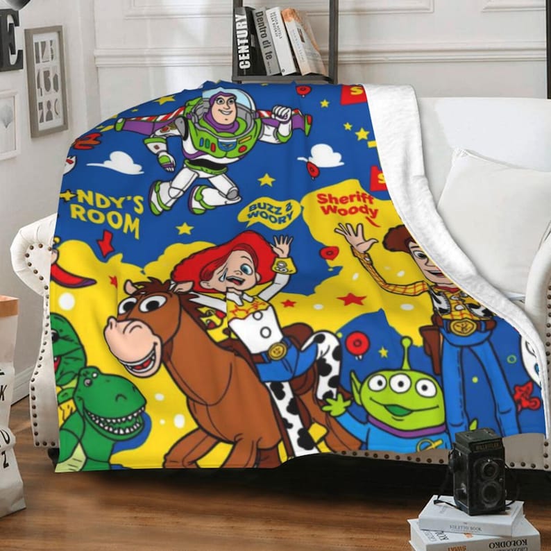 May include: A plush throw blanket featuring a vibrant Toy Story print on a blue and yellow background. The design includes Buzz Lightyear, Jessie riding Bullseye, Sheriff Woody, a green alien, and Rex, with text reading Andy's Room and Buzz & Woody.